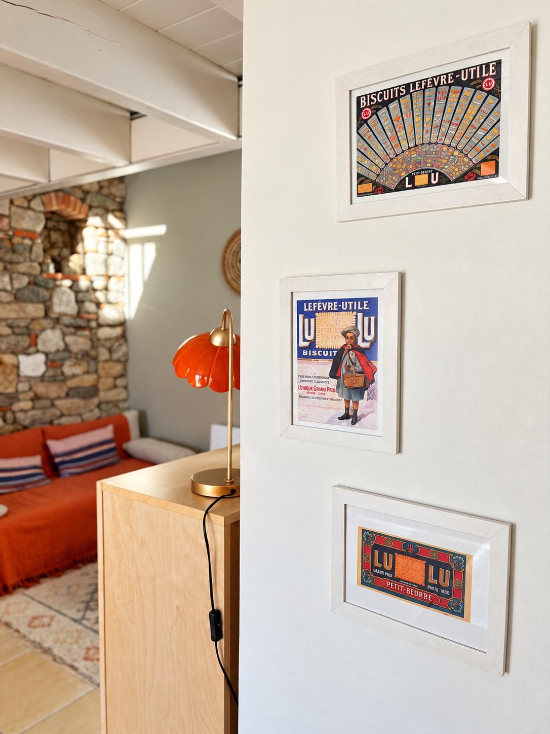Affiches anciennes encadrées sur un mur du séjour, le salon en arrière-plan