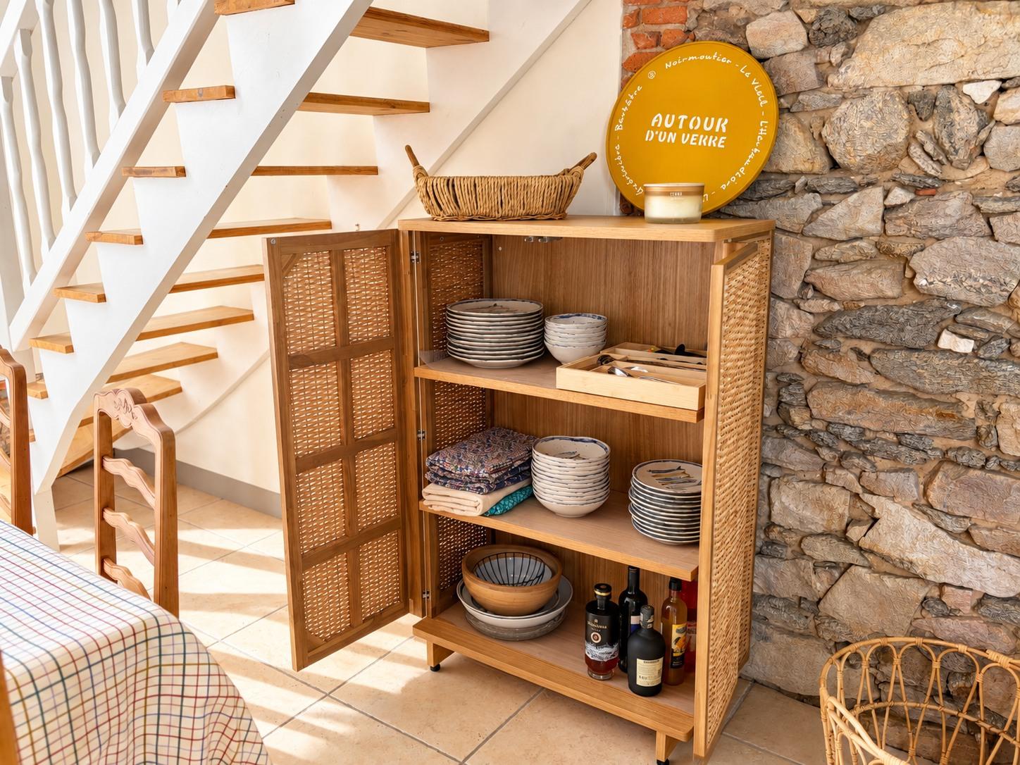 Le buffet en cannage ouvert sur la vaisselle de la maison, contre le mur de pierre