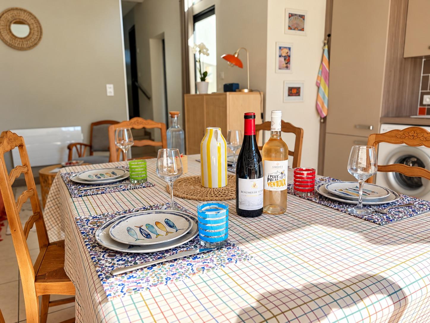 Table dressée dans le séjour : assiettes aux poissons, verres colorés et deux bouteilles de vin