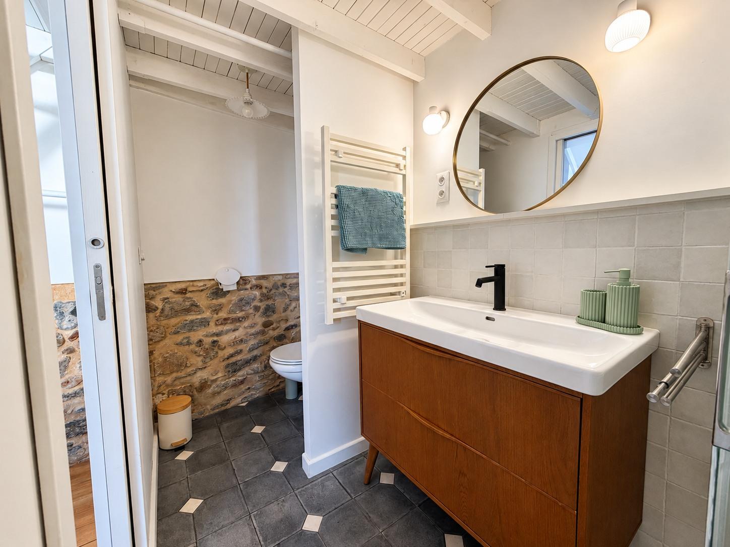 La salle de bain de la dépendance : meuble en bois, miroir rond et robinetterie noire