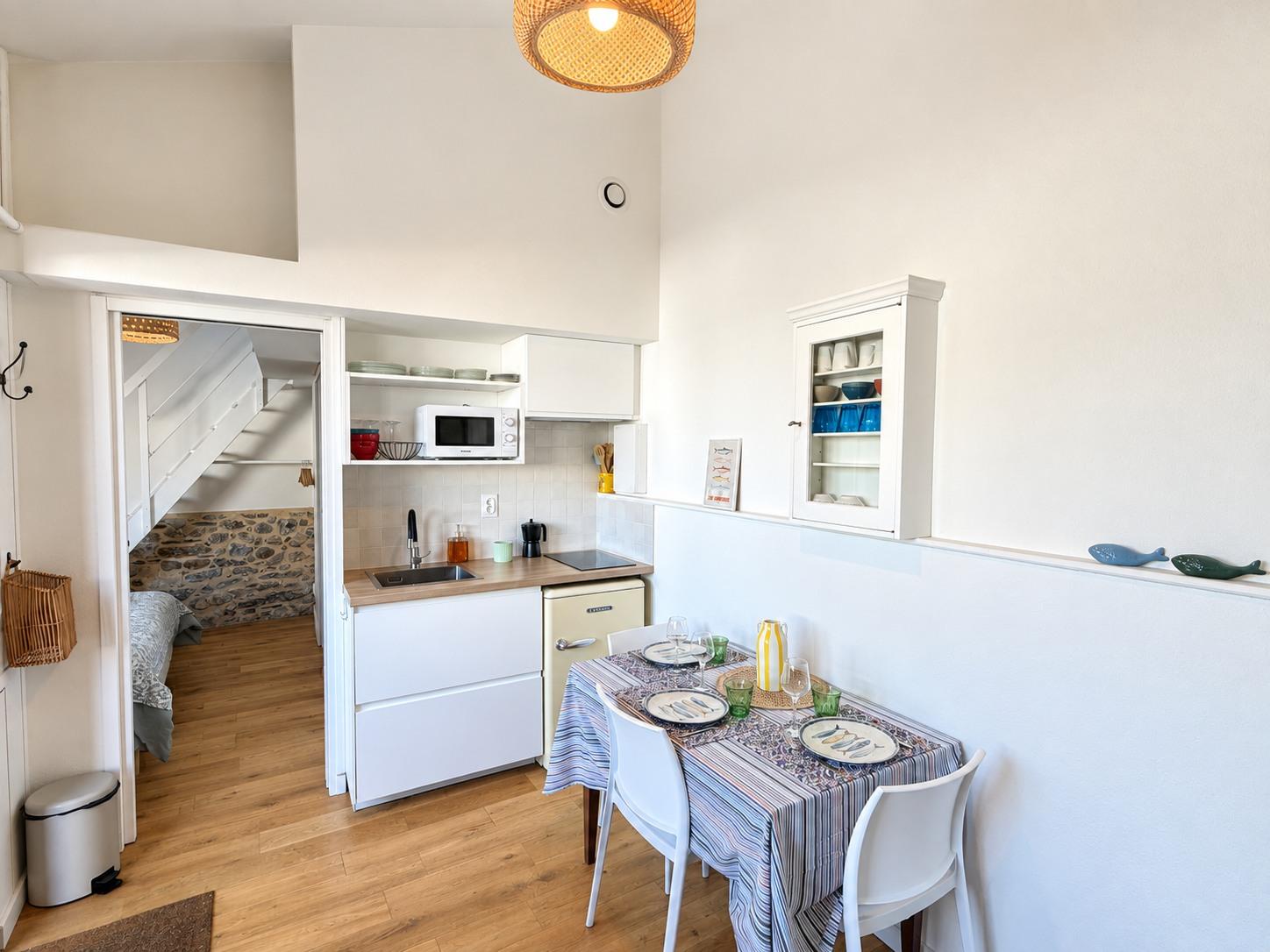 La pièce de vie de la dépendance : kitchenette blanche et table dressée pour quatre