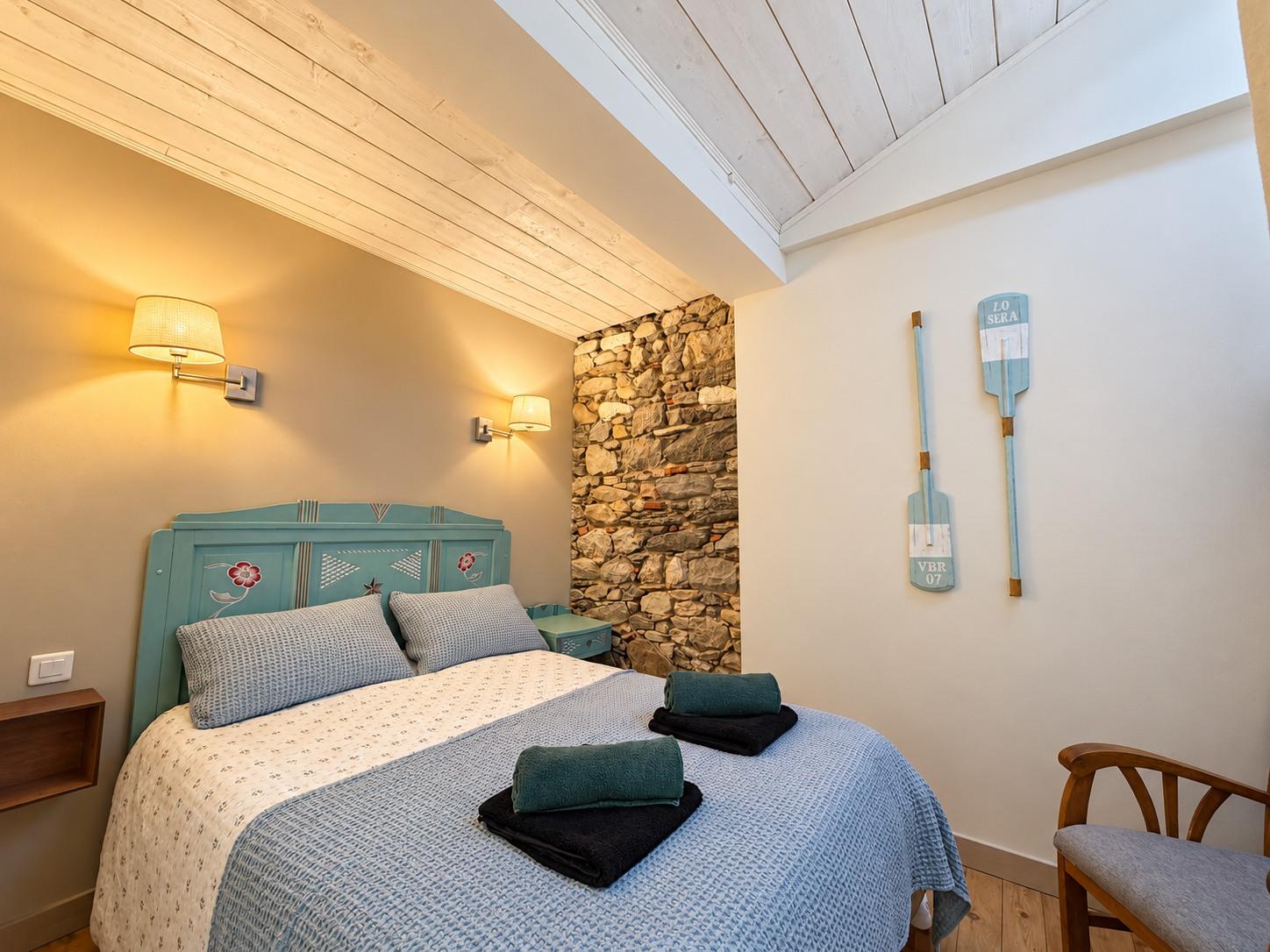Chambre au lit bleu peint et au mur de pierre apparente