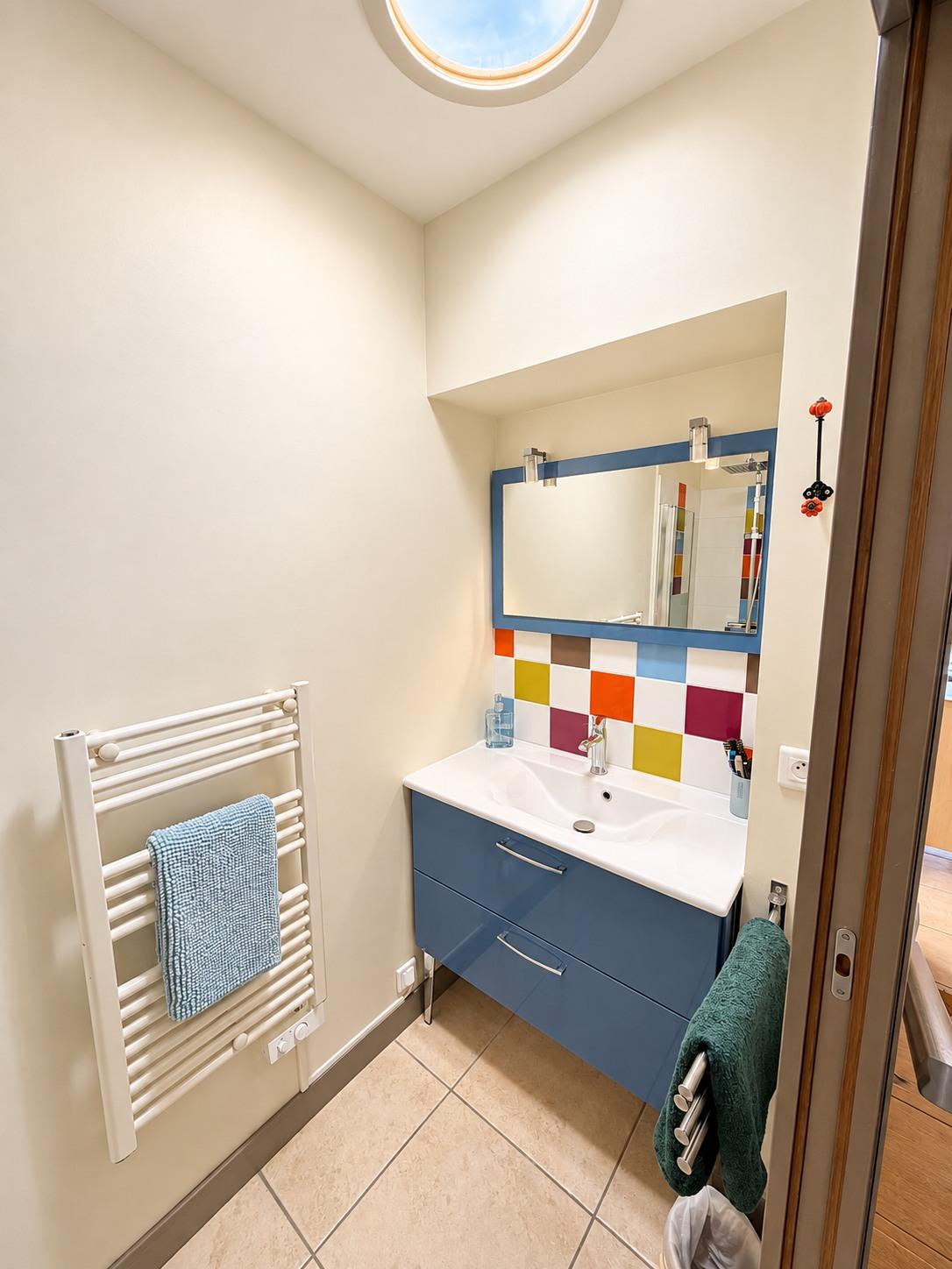 La salle de bain de la maison principale : vasque, miroir bleu et carreaux colorés