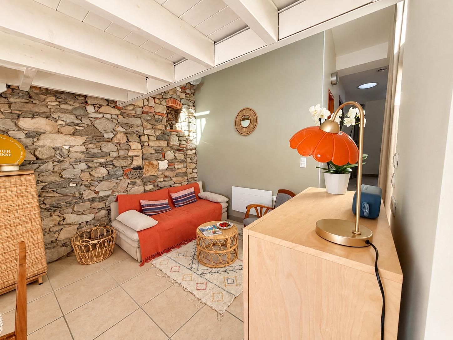 Le coin salon adossé au mur de pierre, avec sa lampe orange et sa table basse en rotin
