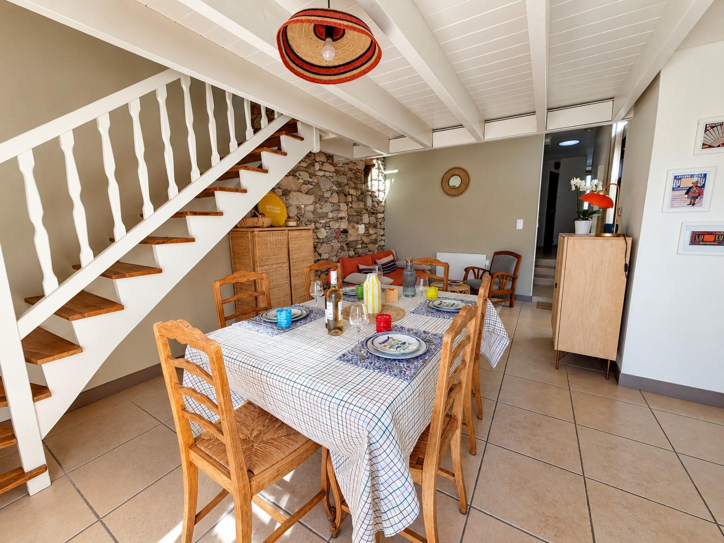 La table du séjour dressée au pied de l'escalier en bois blanc, dans la maison principale